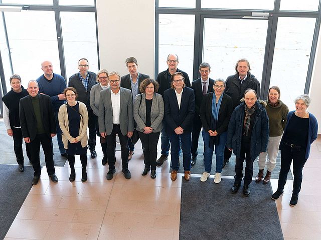 Gruppenbild der Kanzler*innen im Foyer der Hochschule für Musik Nürnberg. Die 17 Kanzler*innen stehen in zwei Reihen hintereinander, das Bild ist von oben aufgenommen. 